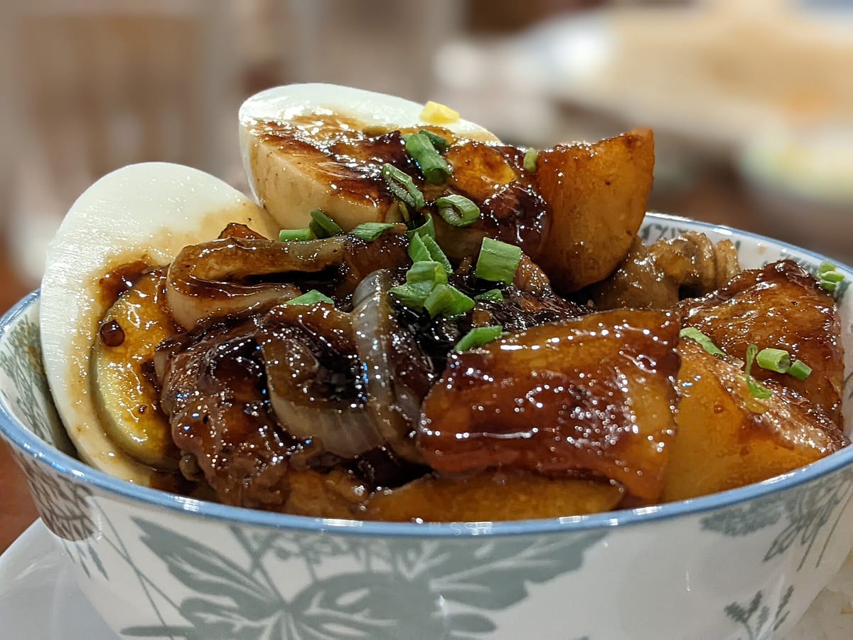 Bowl of glossy chicken adobo with potato chunks and halved eggs