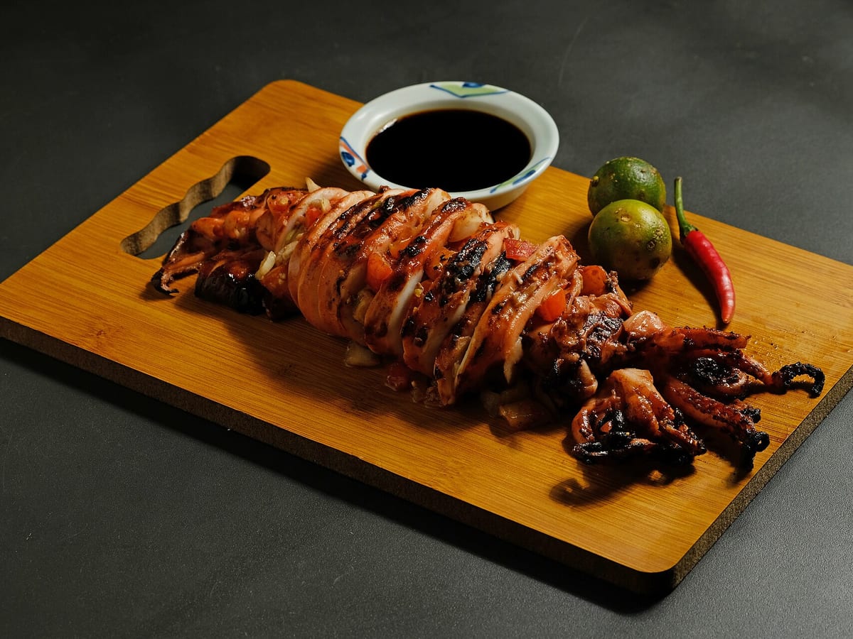 Grilled squid on a wooden board with soy dipping sauce, calamansi and a red chili