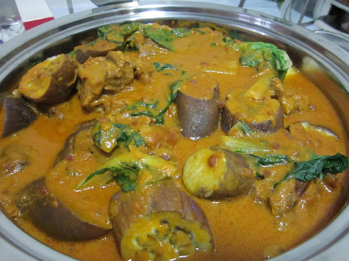 Pan of oxtail kare-kare in golden peanut sauce with eggplant and leafy greens