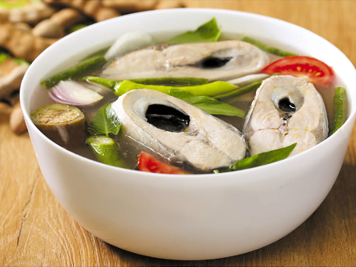 White bowl of sinigang with fish steaks, tomato wedges and green chilies